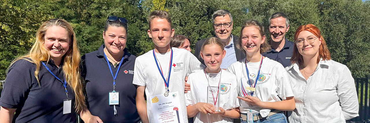 Gruppe von JRK-Mitgliedern mit Urkunde und Plüschtier vor Bäumen