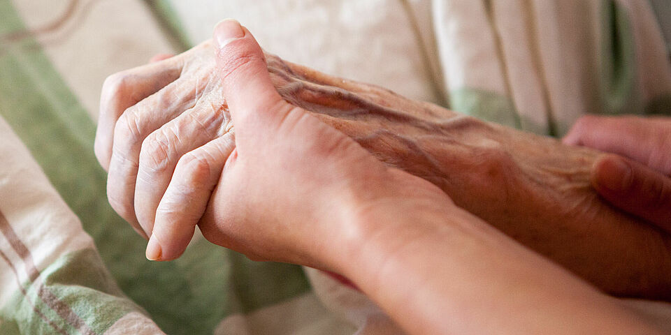 Junge Hände halten die Hand einer alten Person, die im Bett liegt