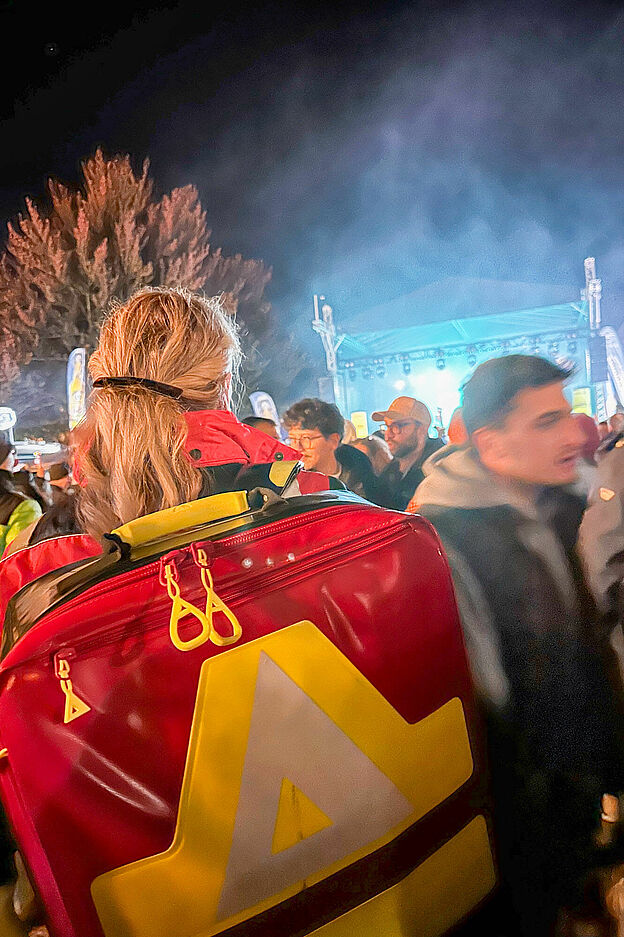 DRK-Sanitäterin mit rotem Notfallrucksack im Besuchergedränge beim abendlichen Zwiebelmarkt in Weimar, im Hintergrund eine beleuchtete Bühne